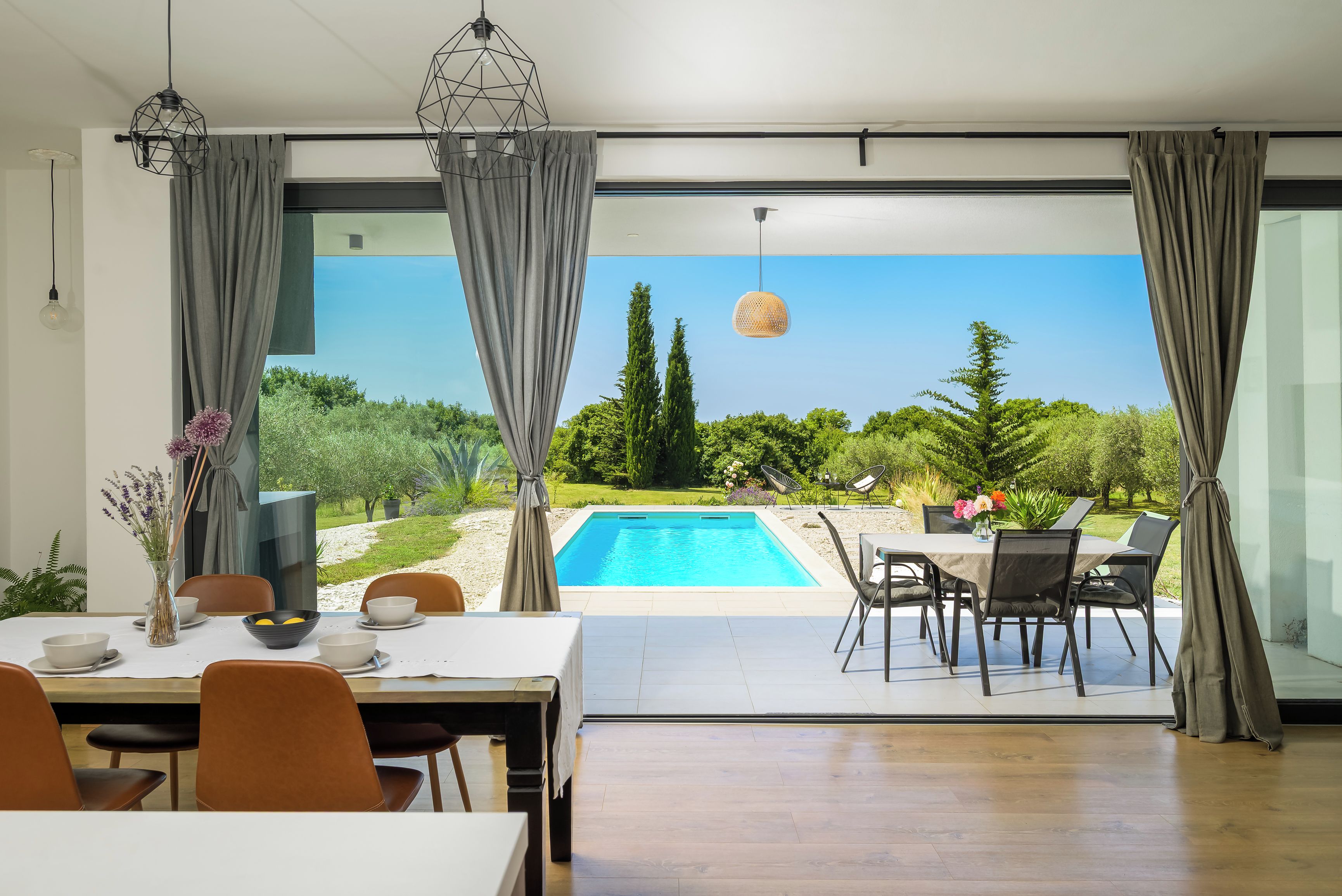 A modern dining area with a view of a swimming pool and garden.