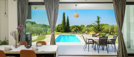 A modern dining area with a view of a swimming pool and garden.