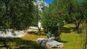 Un jardín con un edificio blanco, follaje verde y una roca.