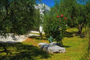 Ein Garten mit einem weißen Gebäude, üppigem Grün und einem Felsen.