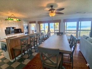 A kitchen with a central island, bar stools, and a view of the ocean through large windows. - Kismet - Oceanfront in Garden City Beach (Garden City Beach)