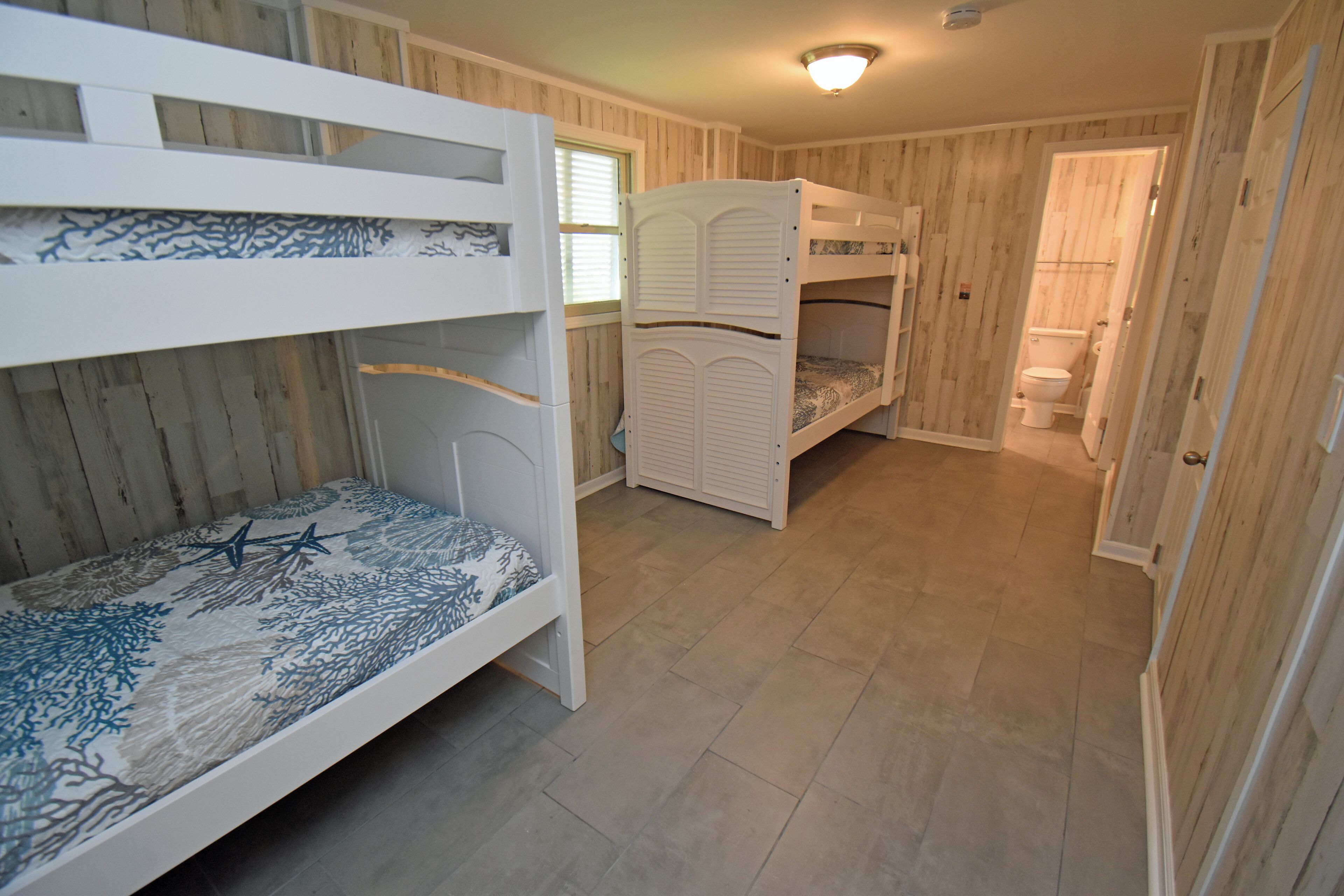 Een kamer met stapelbedden, houten wanden en een betegelde vloer.