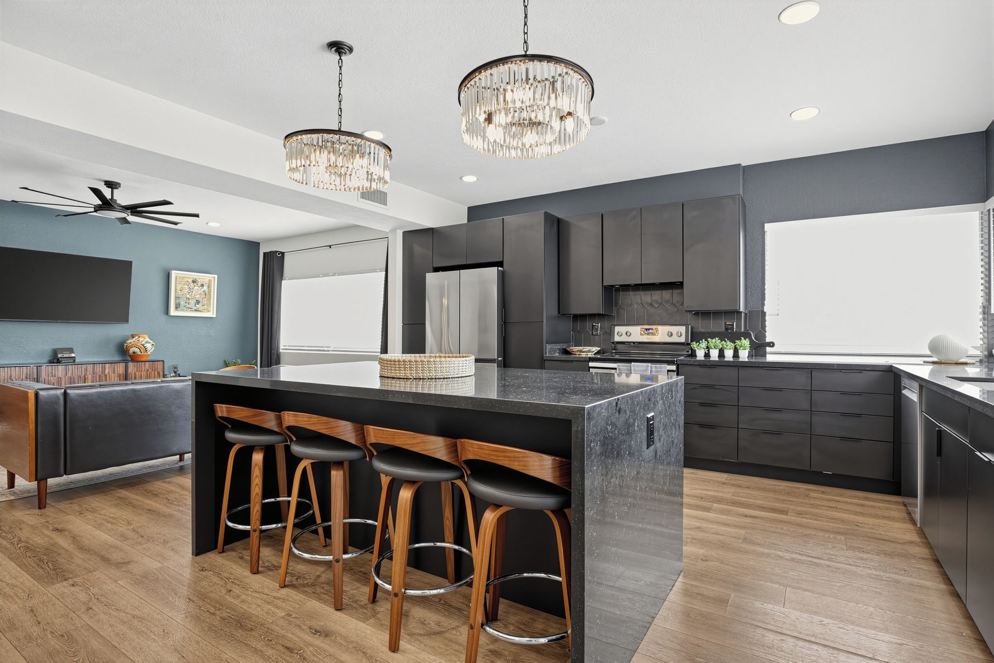 A modern kitchen with a central island, bar stools, a ceiling fan, and pendant lighting.