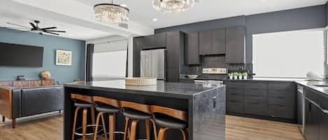 A modern kitchen with a central island, bar stools, a ceiling fan, and pendant lighting.