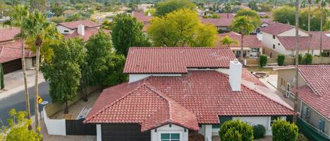 A residential area with houses featuring red-tiled roofs, surrounded by greenery and palm trees.