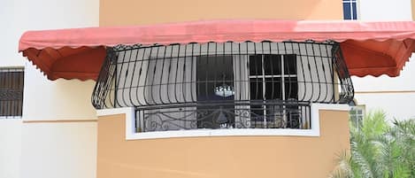 Un edificio de varios pisos con balcones, un toldo rojo y ventanas con rejas.