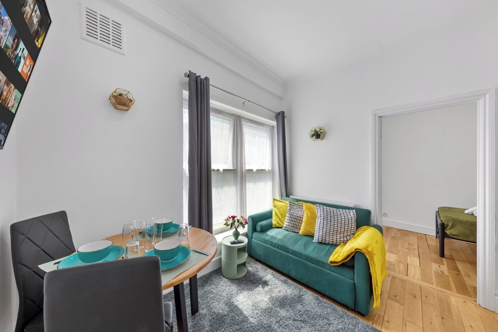 Ein modernes Wohnzimmer mit Essbereich, ein grünes Sofa mit gelben Kissen und ein kleiner Beistelltisch mit einer Vase.