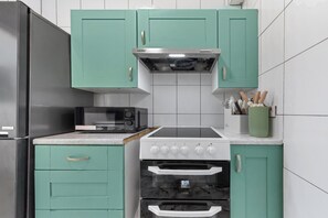 A kitchen with teal cabinets, a microwave, a stove, and an oven. - Modern 2BR Apartment | Sleeps 5 | Canary Wharf E14 (London)