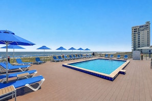 A pool area with lounge chairs and umbrellas, a clear view of the ocean, and a high-rise building in the background. - Luxury Lost Key Retreat | Private Beach Club, Pools & Golf | BEACHBALL PROPERTIES (Pensacola)