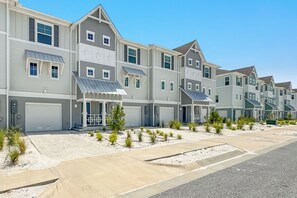 A row of townhouses with attached garages, a paved driveway, and small landscaped areas with shrubs. - Luxury Lost Key Retreat | Private Beach Club, Pools & Golf | BEACHBALL PROPERTIES (Pensacola)