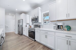 Une cuisine moderne avec des meubles blancs, des appareils en acier inoxydable et un parquet en bois disposé en chevrons.