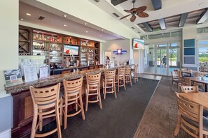 A bar area with a counter, multiple chairs, and a television screen. - Luxury Lost Key Retreat | Private Beach Club, Pools & Golf | BEACHBALL PROPERTIES (Pensacola)