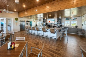 A spacious kitchen with a central island, bar area with stools, and a dining area with wooden tables and chairs. - Luxury Lost Key Retreat | Private Beach Club, Pools & Golf | BEACHBALL PROPERTIES (Pensacola)