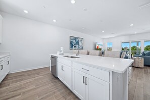 A modern kitchen with a large island, built-in appliances, and a dining area with a view. - Luxury Lost Key Retreat | Private Beach Club, Pools & Golf | BEACHBALL PROPERTIES (Pensacola)