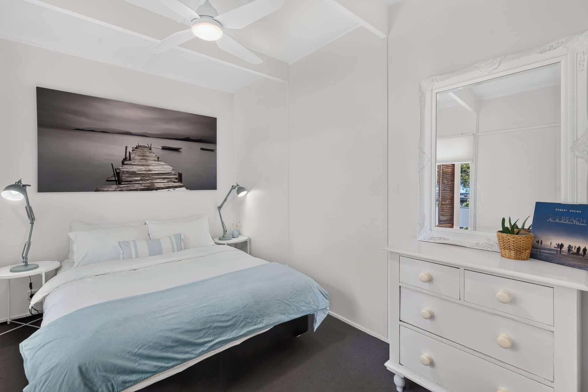 A bedroom with a bed, bedside lamps, a dresser, a mirror, and a framed picture on the wall.