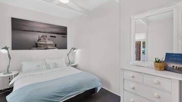 A bedroom with a bed, bedside lamps, a dresser, a mirror, and a framed picture on the wall.
