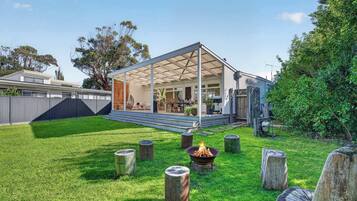 A covered outdoor area with a fire pit, wooden stumps, and a view of a house with a patio.