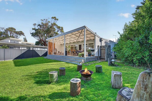 A covered outdoor area with a fire pit, wooden stumps, and a view of a house with a patio.