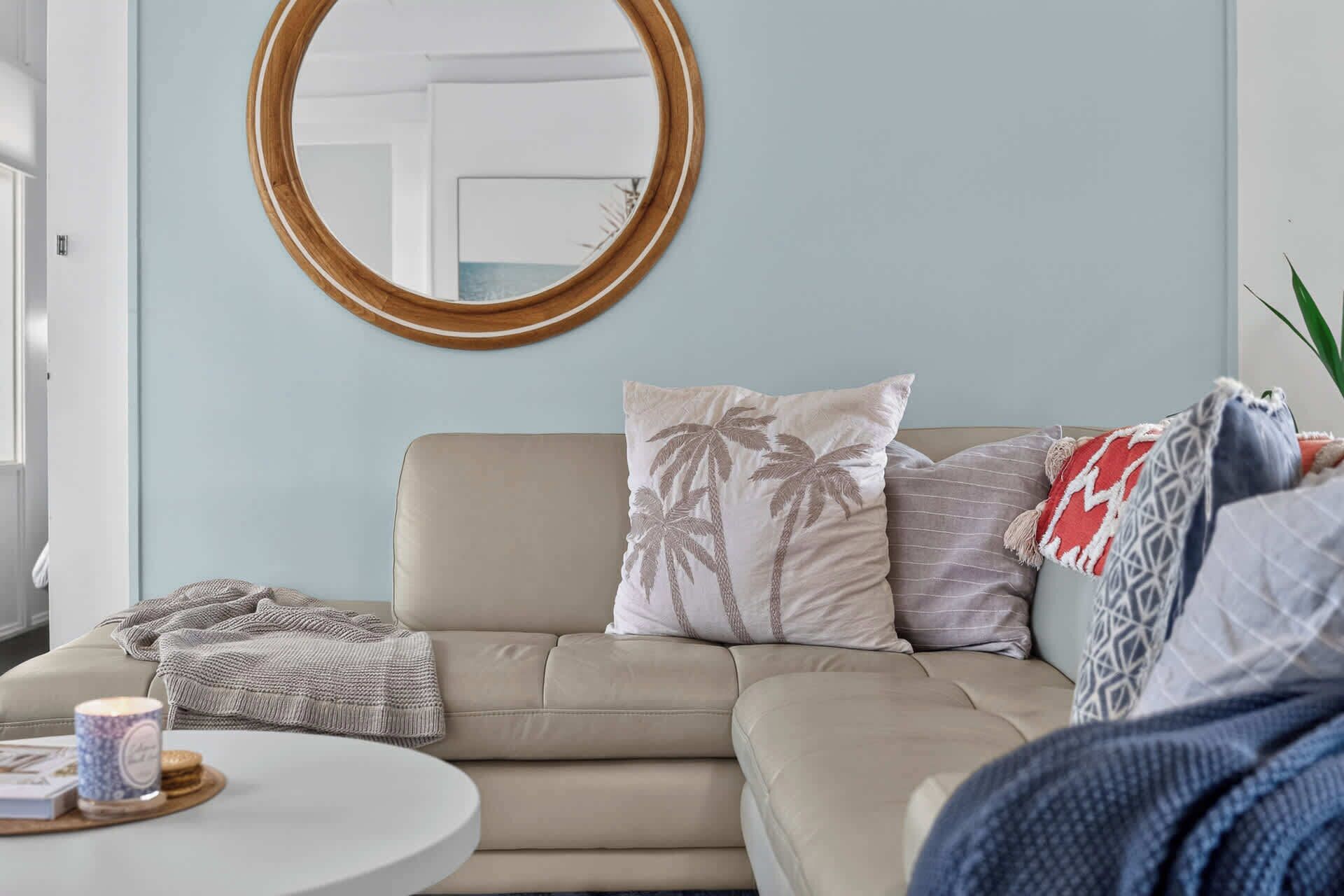 A living room with a beige sofa, a round mirror, and a coffee table with a book and a candle.
