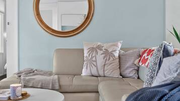 A living room with a beige sofa, a round mirror, and a coffee table with a book and a candle.