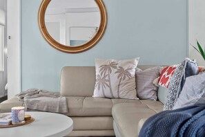 A living room with a beige sofa, a round mirror, and a coffee table with a book and a candle.