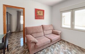 A room with a pink sofa, a wooden-framed mirror, a red artwork, and a window with blinds. - Lovely apartment in Los Alcázares with WiFi (Los Alcázares)