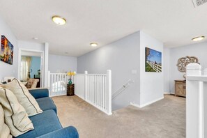 Een ruime woonkamer met een blauwe bank, een witte balustrade en kunst aan de muren.