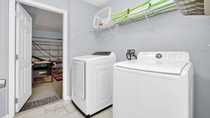 A laundry room with two white washing machines, a white dryer, and a wall-mounted drying rack with folded towels.