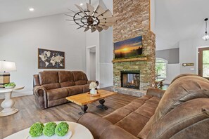 A modern living room with a stone fireplace, leather sofas, a wooden coffee table, and a world map artwork. - Summit Trails Sanctuary: 3bdrm. Sleeps 8, Hot Tub, One level, Pool Table (Sevierville)