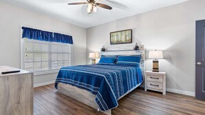 Ein Schlafzimmer mit einem Bett, Nachttischen, einem Deckenventilator, einem Fenster mit Jalousien und einer Tür.