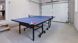 A ping pong table with a ball and paddle in a garage-like space with a concrete floor and a garage door in the background. - Summit Trails Sanctuary: 3bdrm. Sleeps 8, Hot Tub, One level, Pool Table (Sevierville)