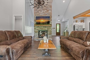 A spacious living room with a stone fireplace, leather sofas, and a wooden coffee table. - Summit Trails Sanctuary: 3bdrm. Sleeps 8, Hot Tub, One level, Pool Table (Sevierville)