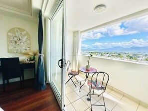 A balcony with a table and chairs, a view of the cityscape, and a decorative wall piece. - Prime CBD Studio | City & Mountain Views (Cairns City)