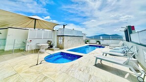 Zona de piscina en la azotea con cielo despejado, piscina, sillas de descanso y un área de estar cubierta.