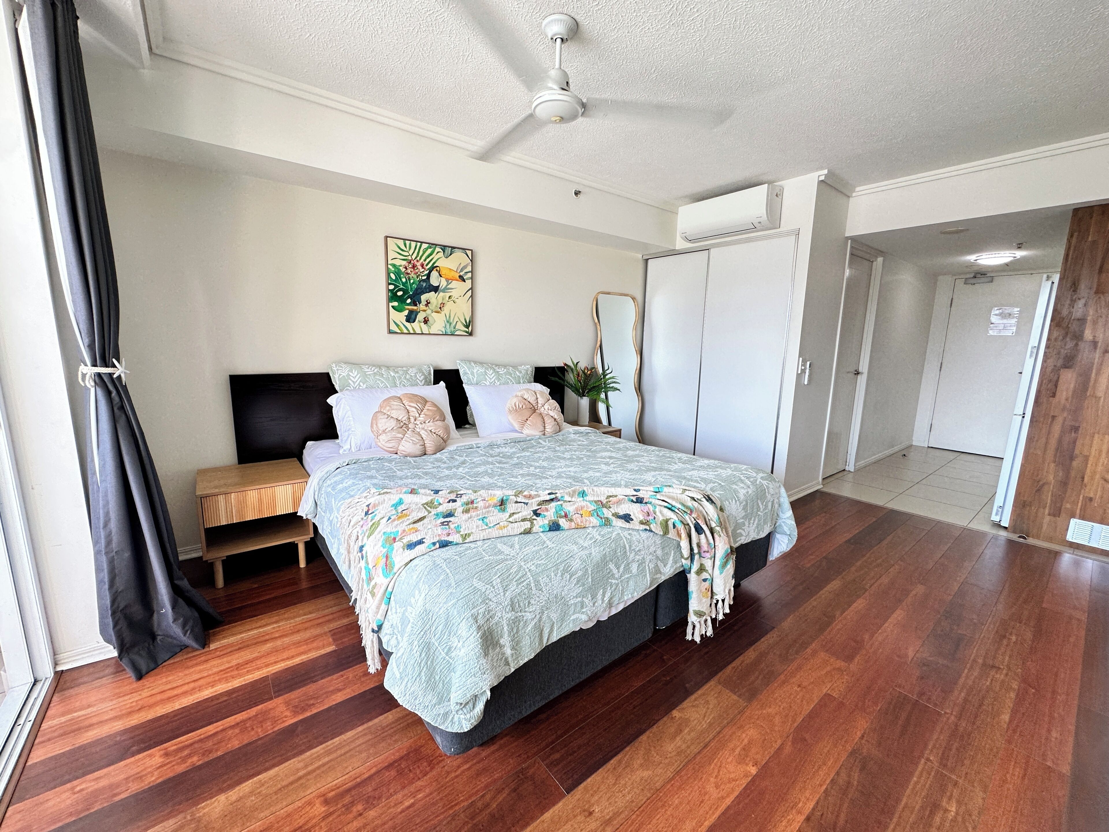 A bedroom with a bed, a ceiling fan, a door, and a window with curtains.