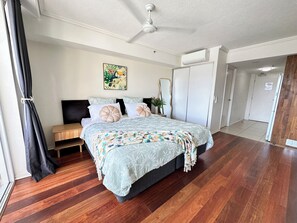 A bedroom with a bed, a ceiling fan, a door, and a window with curtains. - Prime CBD Studio | City & Mountain Views (Cairns City)