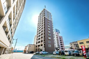 Um edifício de vários andares com um eixo de elevador central, cercado por carros estacionados e prédios menores.