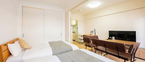Et hotelværelse med to senge, et spiseområde med bord og stole, et fjernsyn og et tekøkken.
