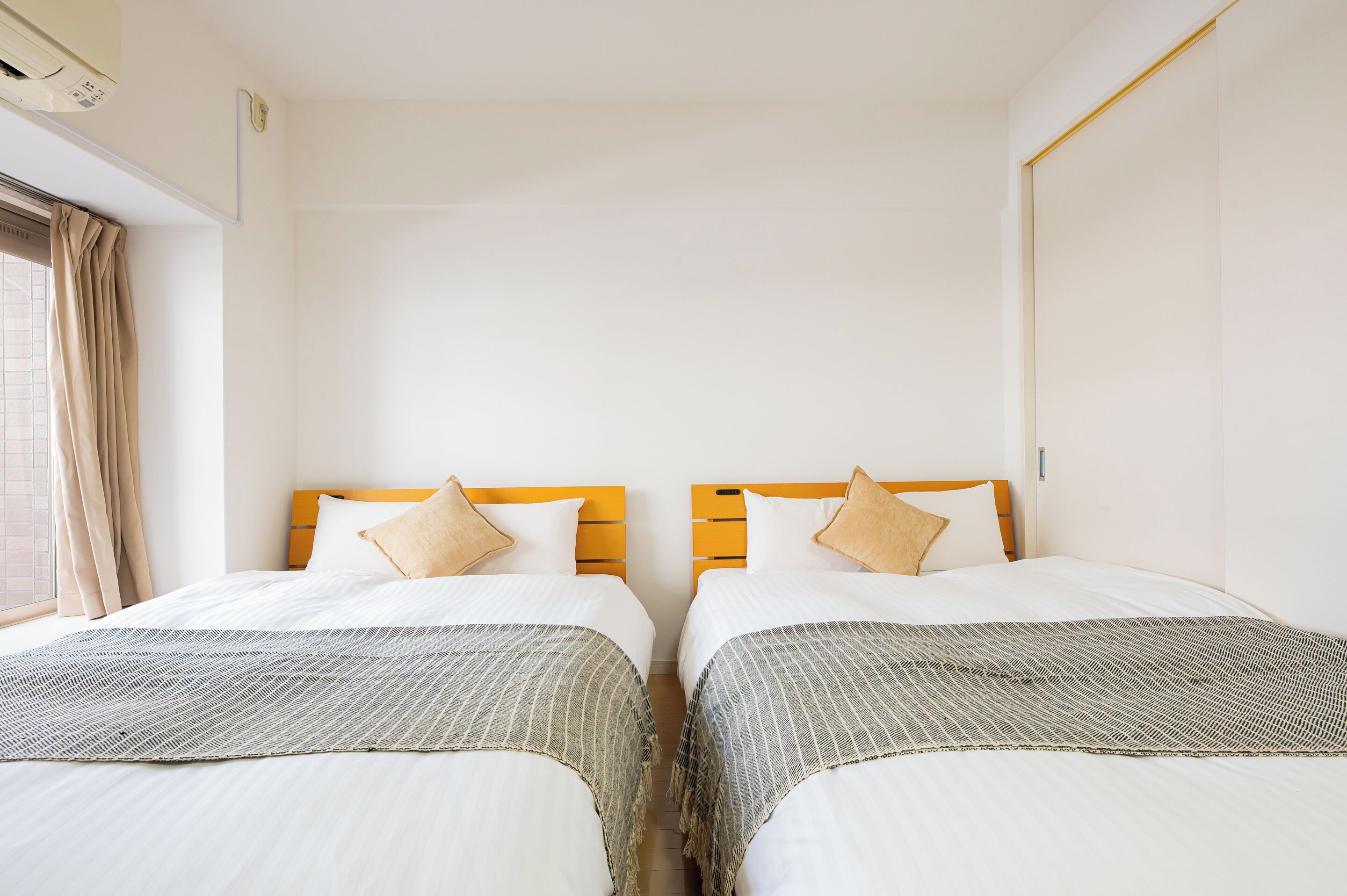 A hotel room with two beds, each with a wooden headboard, white bedding, and a patterned throw.