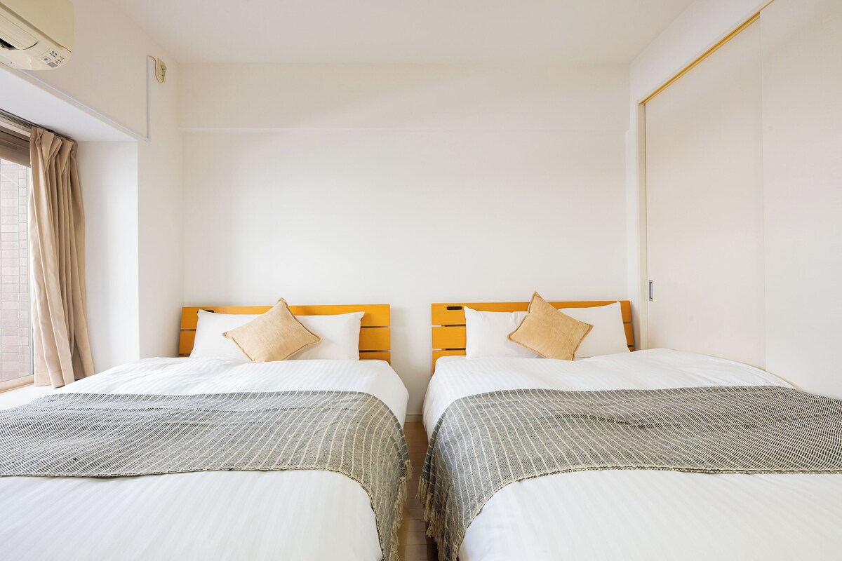 Een hotelkamer met twee bedden, elk voorzien van een houten hoofdeinde, witte beddengoed en een decoratief plaid.