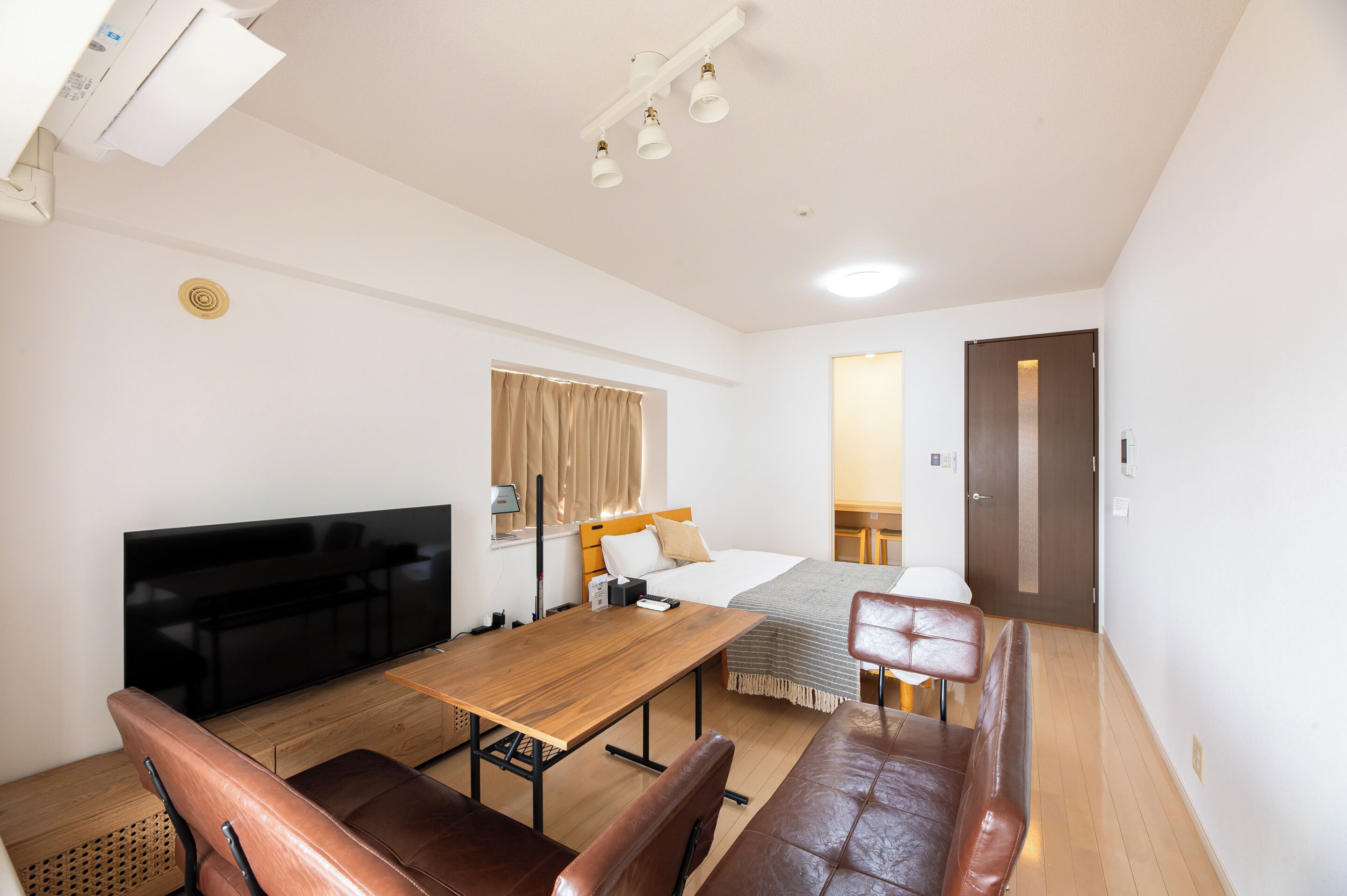 A hotel room with a bed, a desk, a TV, a seating area, and a door.