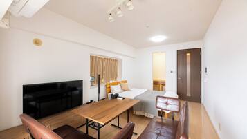 A hotel room with a bed, a desk, a TV, a seating area, and a door.