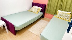 Una habitación pequeña con dos camas individuales, una silla blanca y una lavadora.