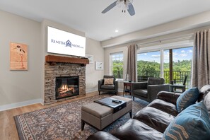 A living room with a fireplace, a mounted television, and a view of a balcony. - Lake Taneycomo Front Condo Minutes to Branson Landing_Shared Outdoor Pool_Free Attraction Tickets (Branson)