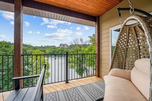 Ein Balkon mit Hängesessel, Holzterrasse und Blick auf einen Fluss und Bäume.
