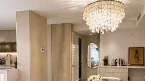 A modern dining area with a glass-top table, white upholstered chairs, a decorative chandelier, and a mirror on the wall. - 2-bedroom apartment in fantastic Fort Lauderdale beach walking distance (Fort Lauderdale)