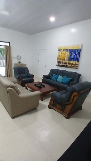 Uma sala de estar com sofá, poltronas, mesa de centro e um quadro na parede.