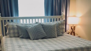 Una camera da letto con un letto bianco, tende blu, una ventola a soffitto e un comodino con una lampada.