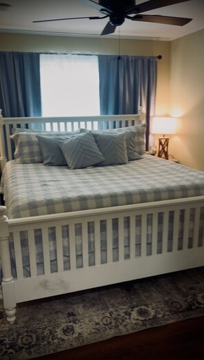 Ein Schlafzimmer mit einem weißen Bett, blauen Vorhängen, einem Deckenventilator und einem Nachttisch mit Lampe.