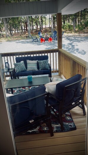 A covered outdoor seating area with a table and chairs, a fire pit, and a view of a forested area.